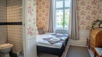 A bathroom with a toilet, a shower area, and a bed with floral wallpaper and a window.
