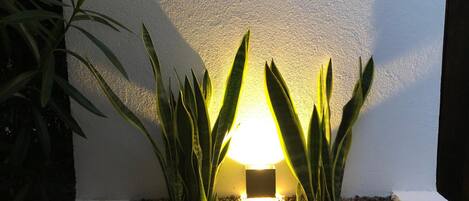 A planter box with a small light fixture, surrounded by green plants and pebbles.