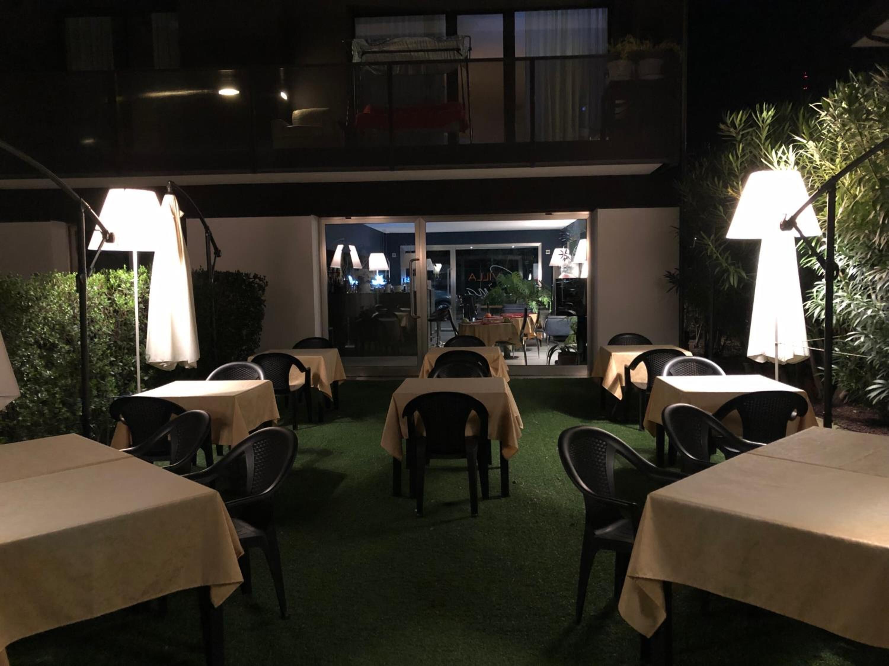An outdoor dining area with tables and chairs, covered by umbrellas, and a view of the interior restaurant through a glass door.