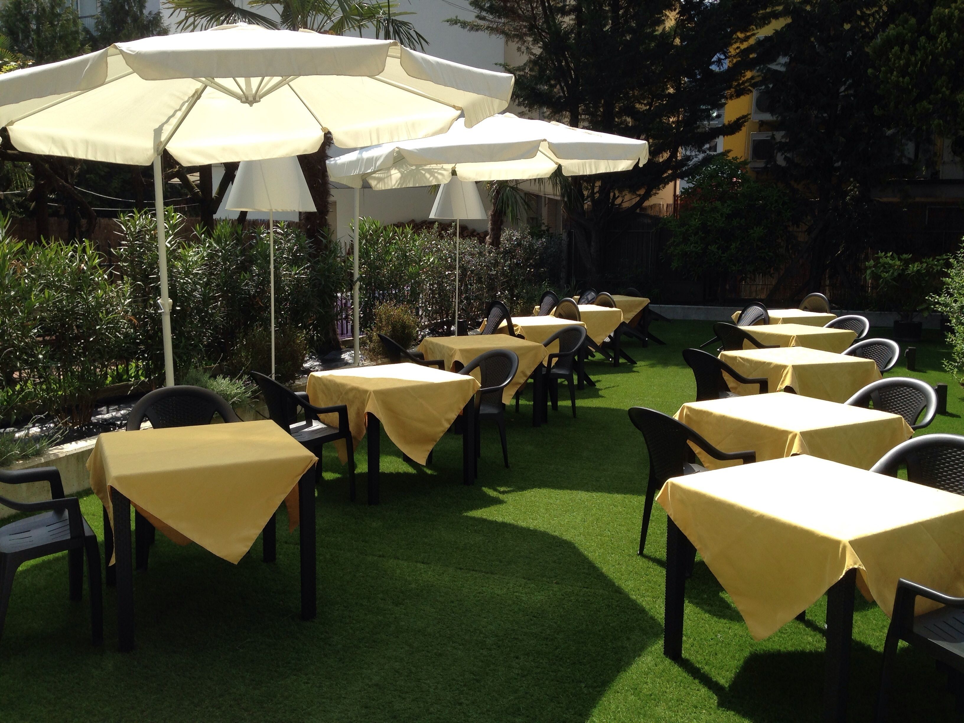 Een buitenterras met tafels en stoelen, beschut door parasols, gelegen op kunstgras.
