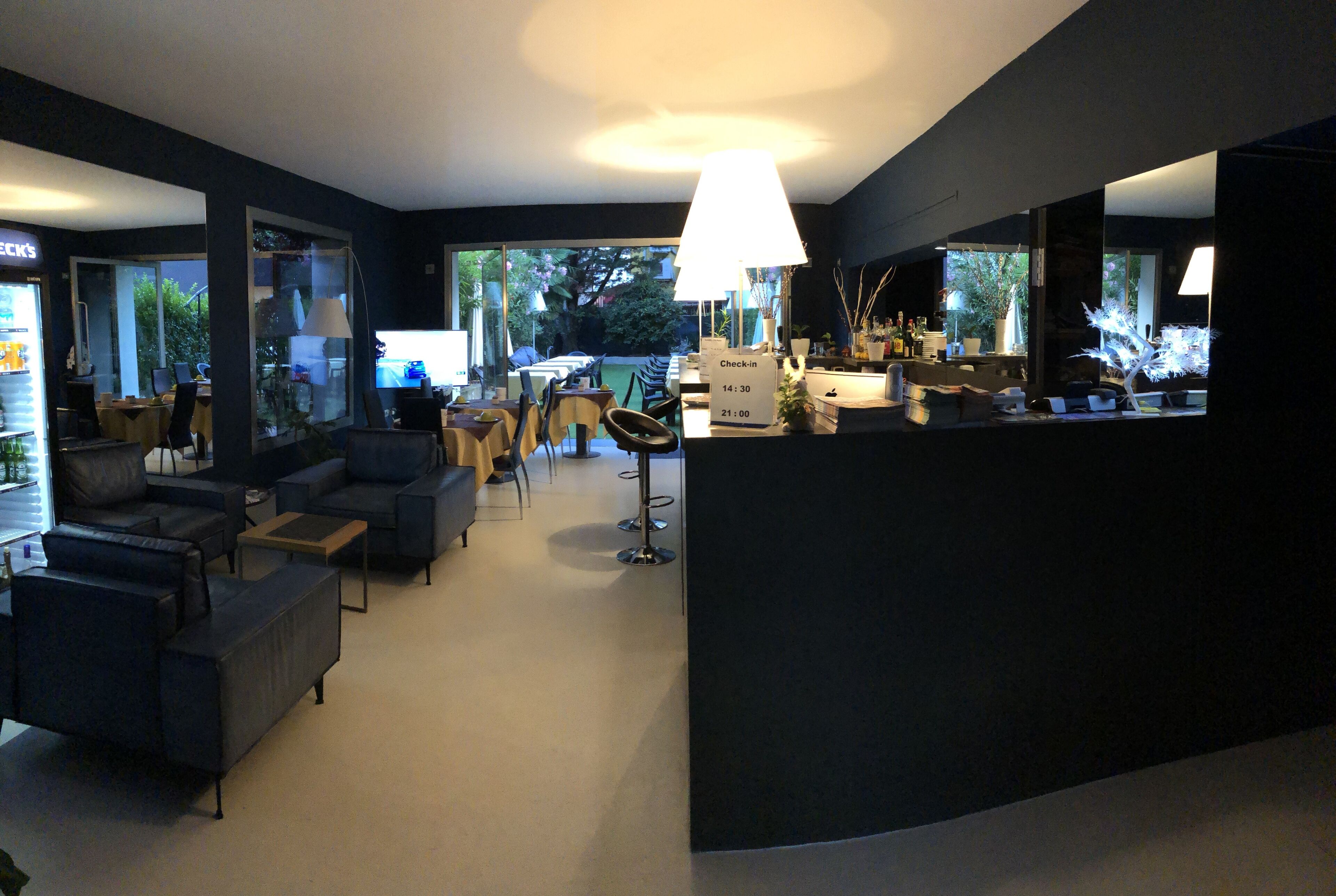 A modern living room with dark sofas, a coffee table, and a dining area with chairs and a table. There is a large window providing a view of the outdoors.