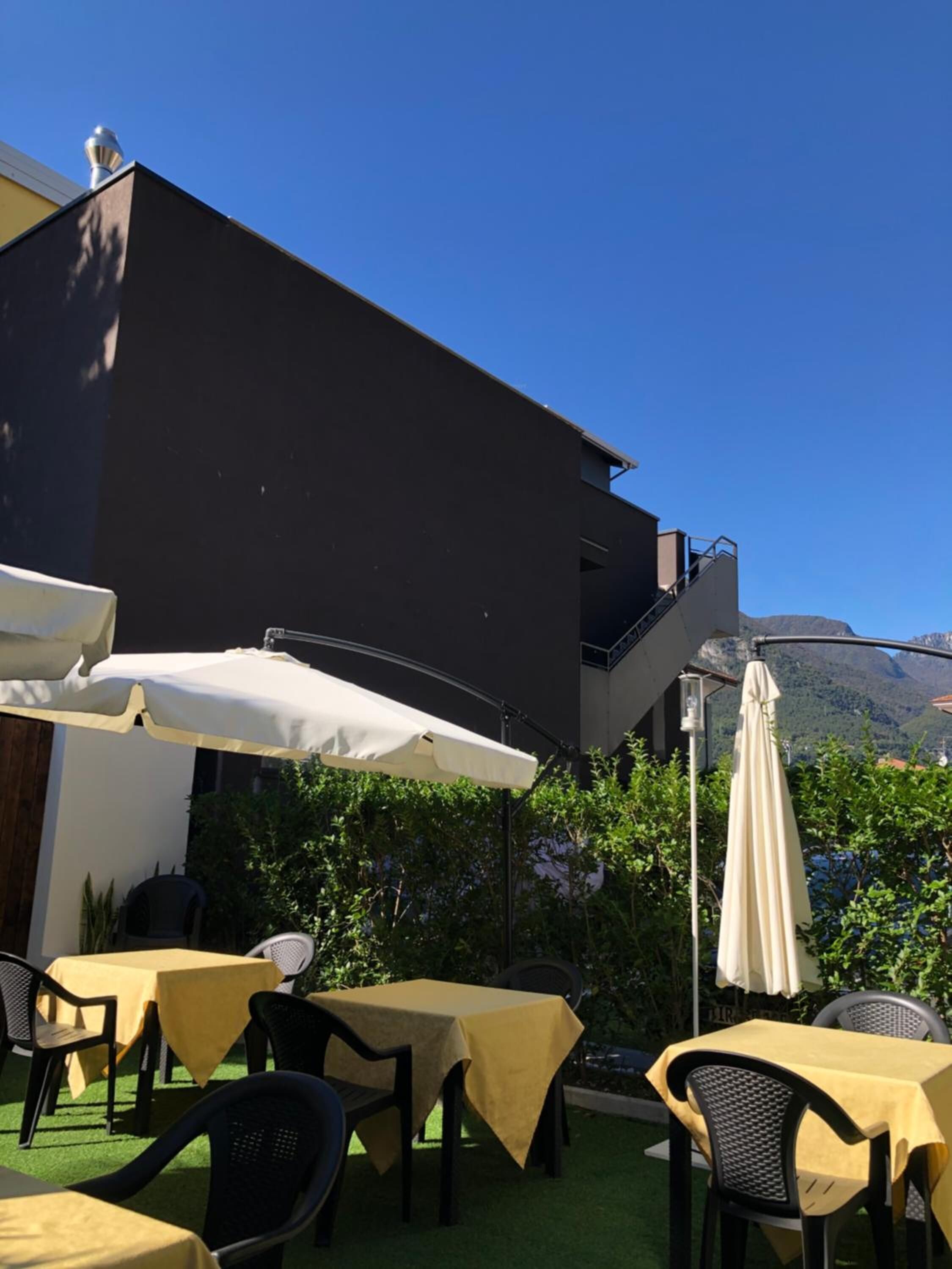 Terrassa exterior amb taules i cadires, un edifici al fons i vista a les muntanyes.