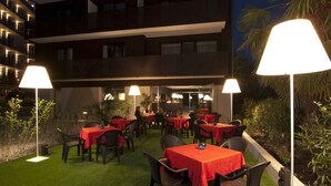 An outdoor dining area with tables and chairs, surrounded by greenery and illuminated by lamps. - Villa Regina (Riva del Garda)