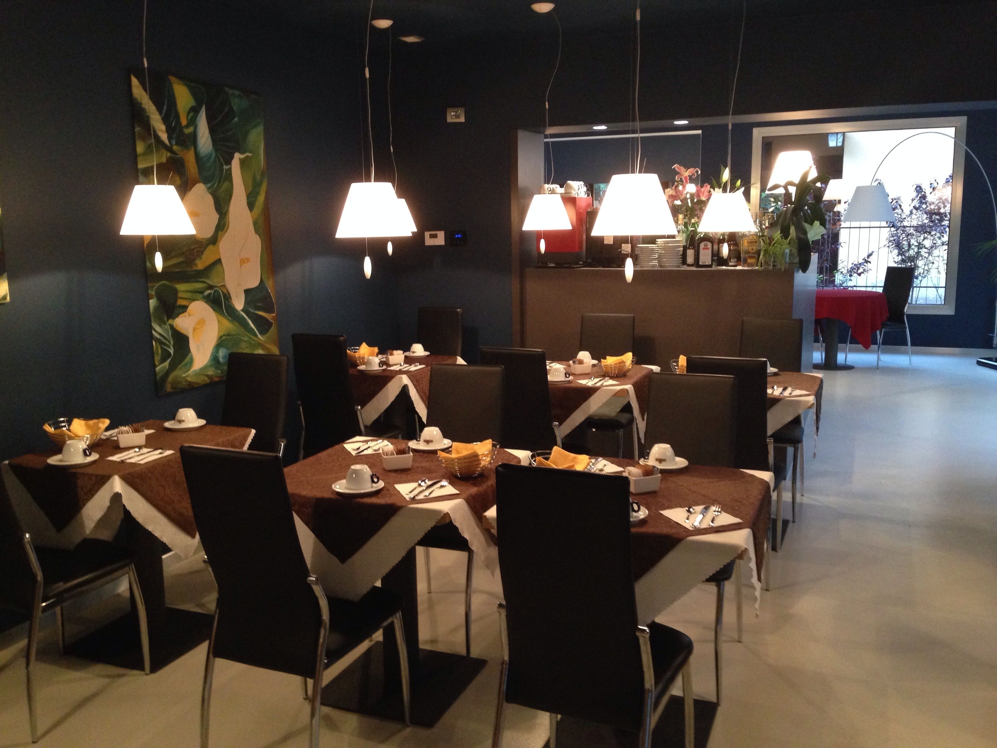 A dining area with tables set for service, chairs, and hanging lamps.