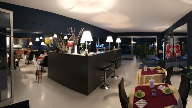 A modern dining area with a central island, multiple tables, and chairs. There is a dog visible in the foreground. - Villa Regina (Riva del Garda)