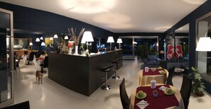 A modern dining area with a central island, multiple tables, and chairs. There is a dog visible in the foreground. - Villa Regina (Riva del Garda)