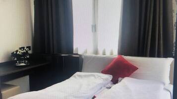A hotel room with a bed, a desk, and a window with curtains.