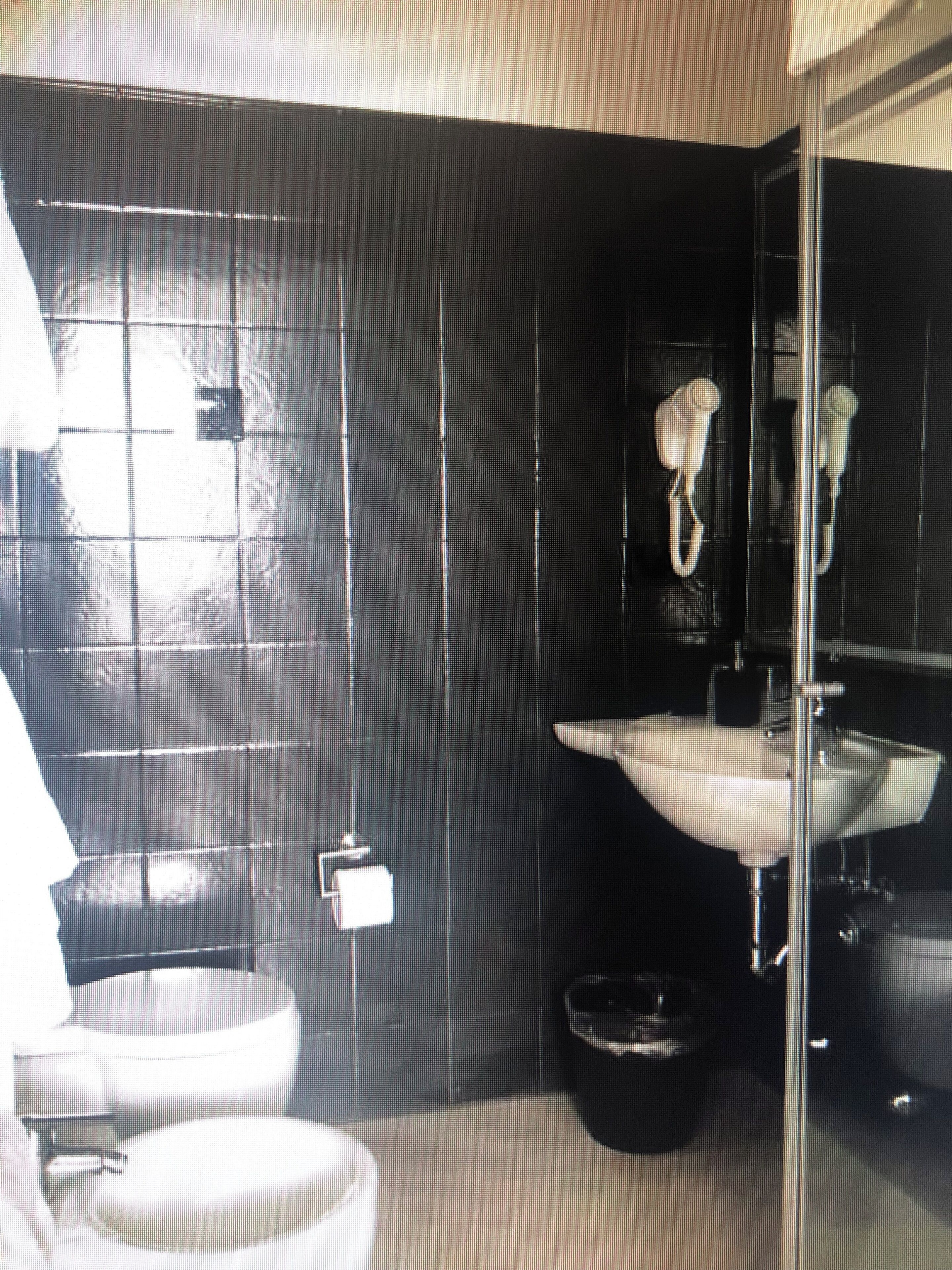 Un baño con pared de azulejos negros, un lavabo blanco, un espejo y una toalla colgada.