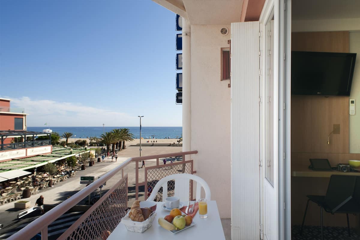 A balcony with a breakfast setup overlooking a beach.