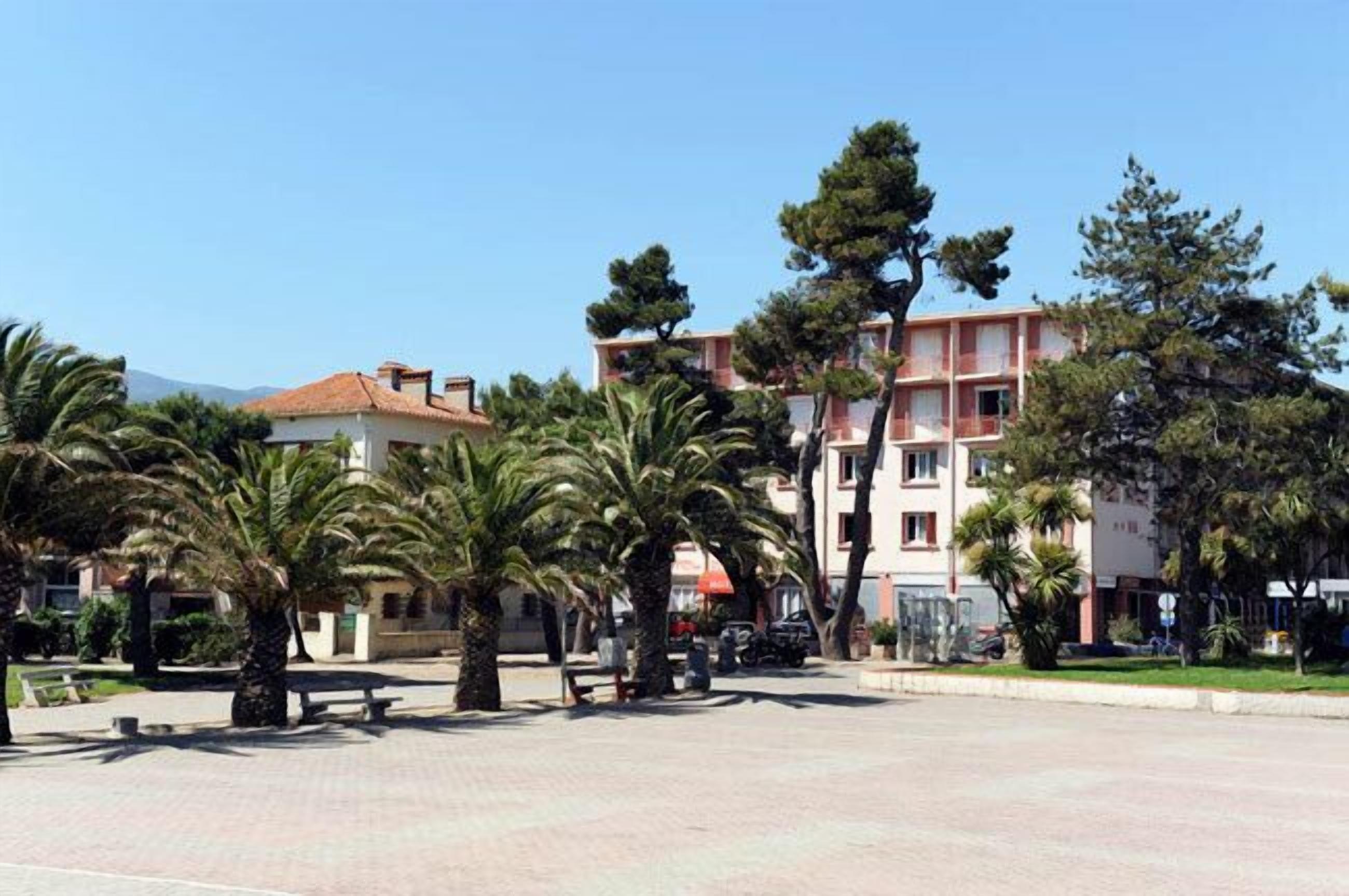 A courtyard with palm trees, benches, and buildings with balconies.