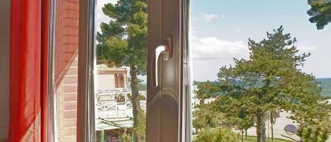 A window with a view of a building with a balcony and trees.