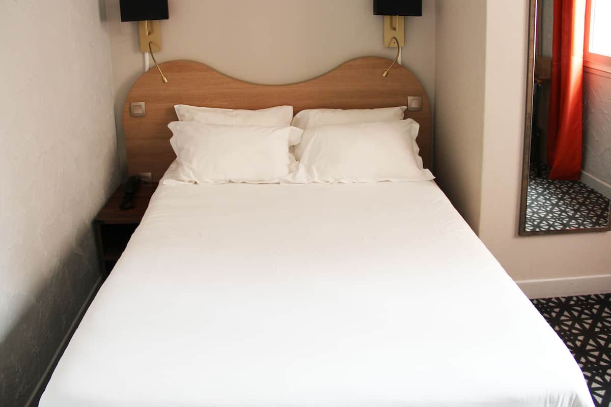 A neatly made bed with white linens and two pillows, a wooden headboard, bedside lamps, and a nightstand with a phone.