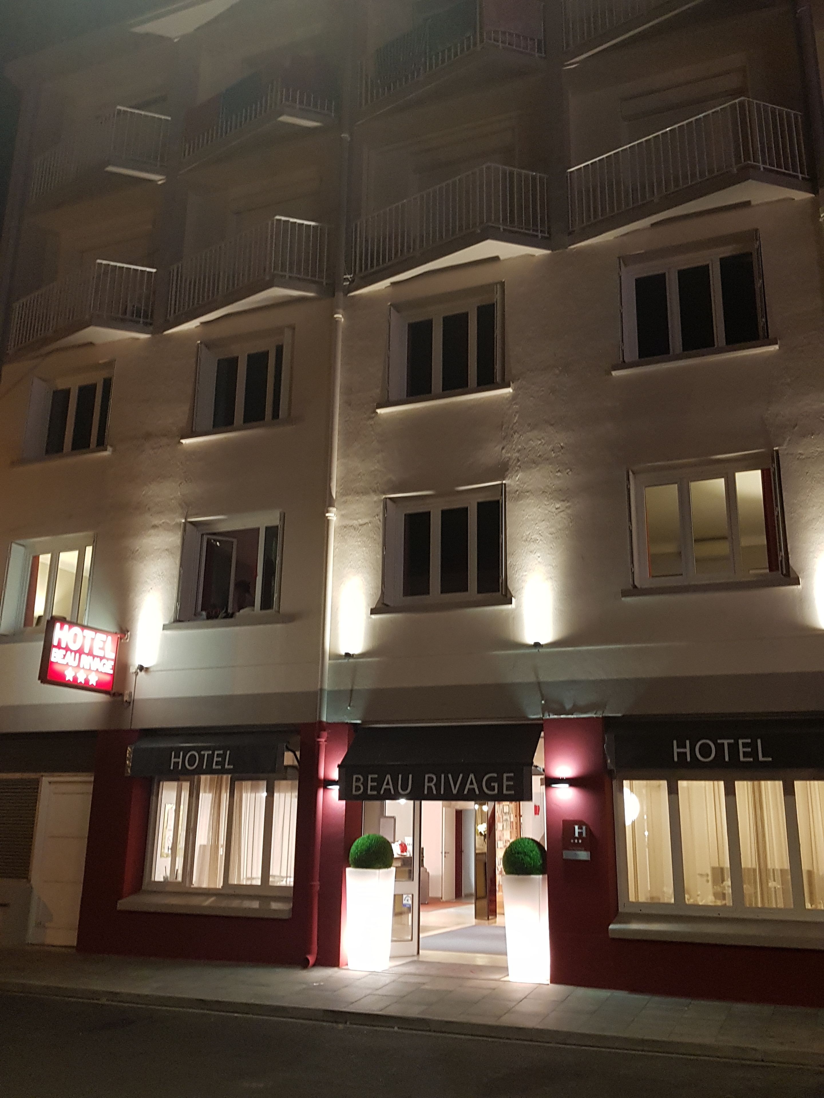 Fachada de hotel iluminada de noche, con señalización brillante, varios balcones y grandes ventanales.