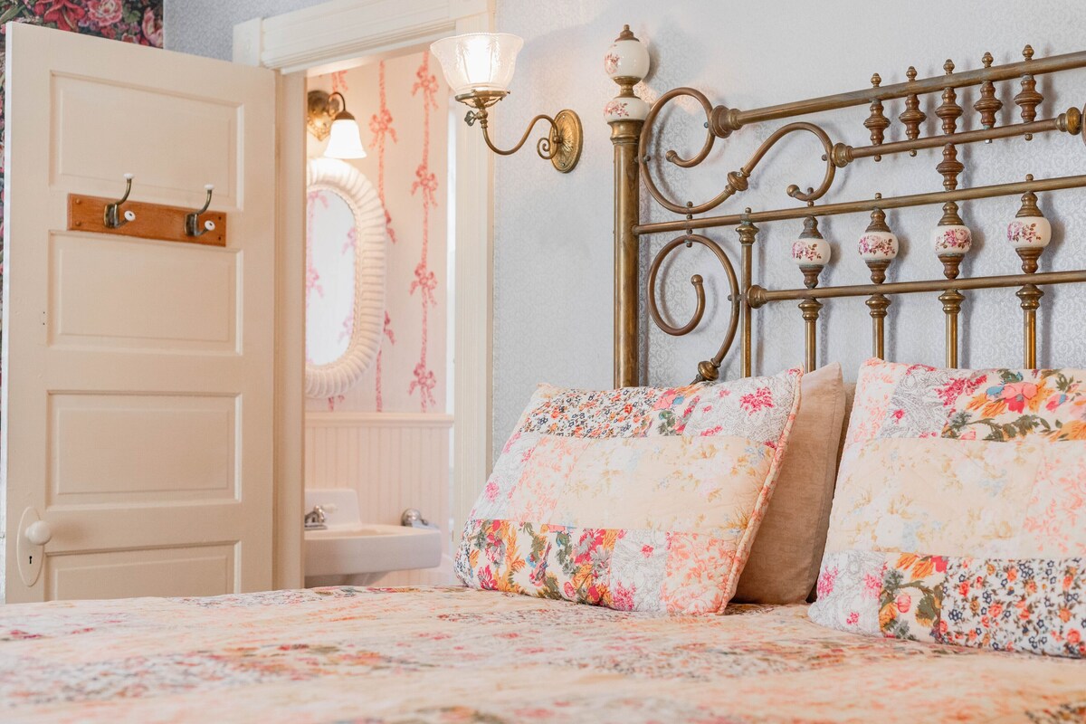 A bedroom with a floral bedspread, a white door, and a wall-mounted light fixture.