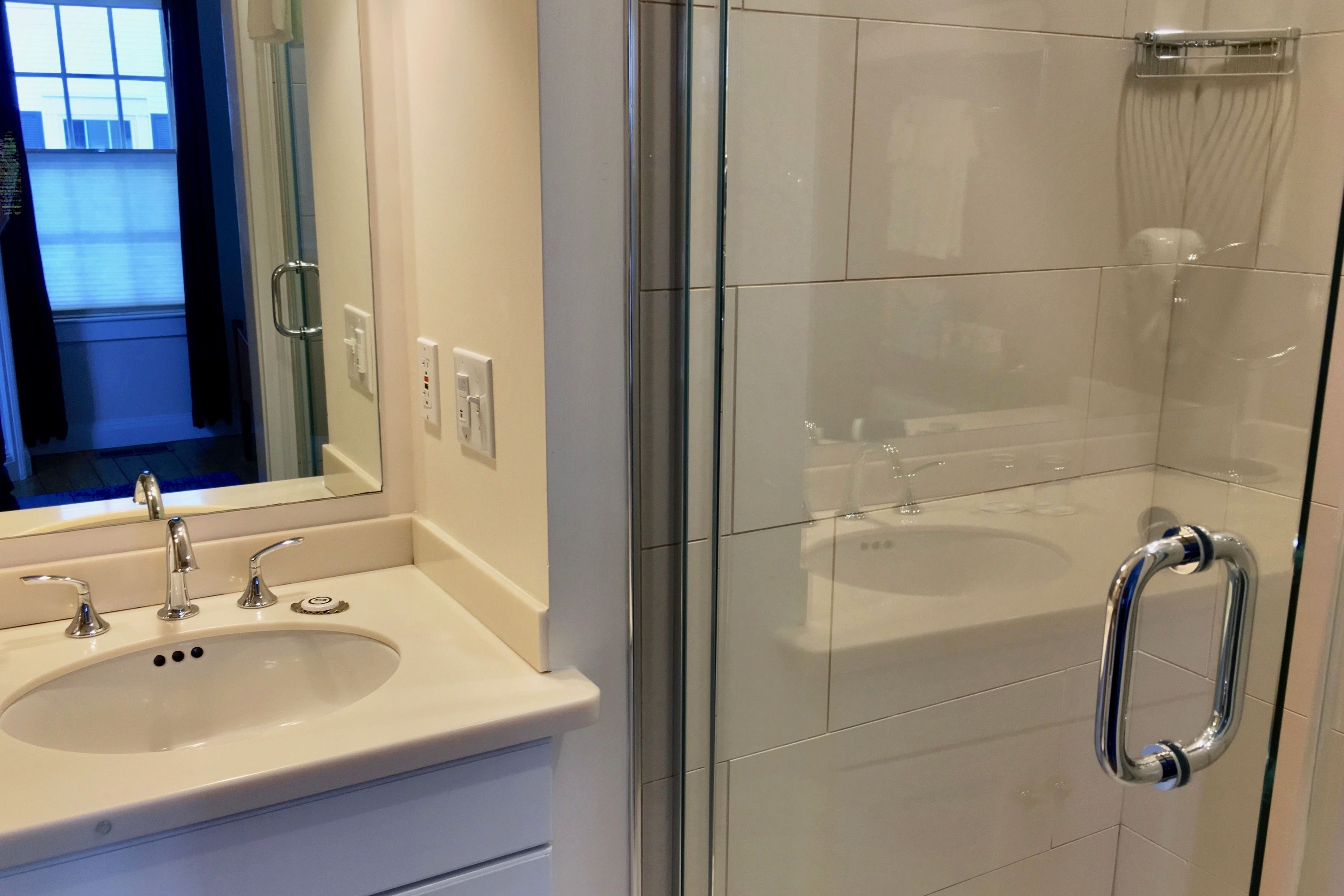 A modern bathroom with a glass shower enclosure, a white sink with a mirror, and a towel rack.