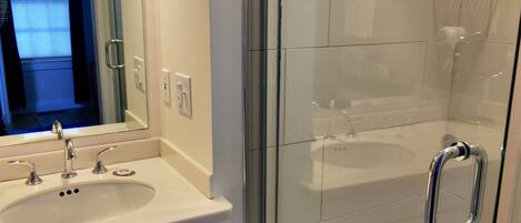 A modern bathroom with a glass shower enclosure, a white sink with a mirror, and a towel rack.