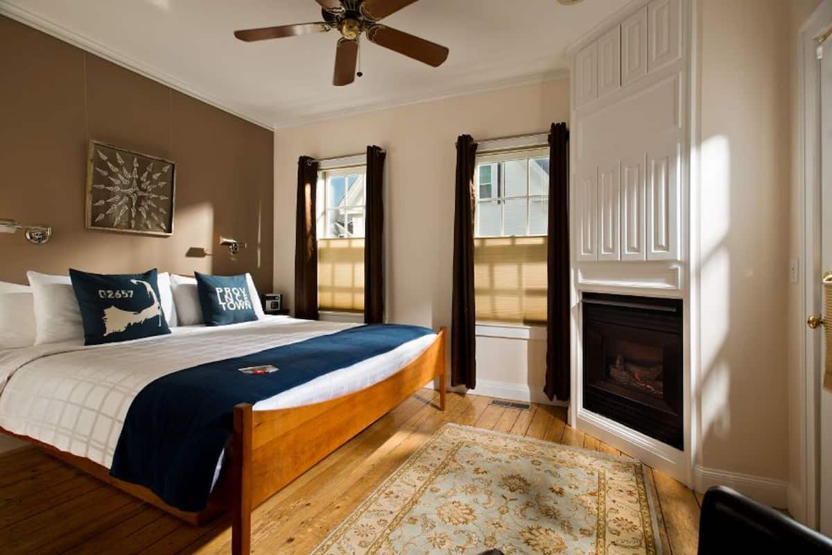 A bedroom with a wooden bed, a ceiling fan, a fireplace, and a window with curtains.