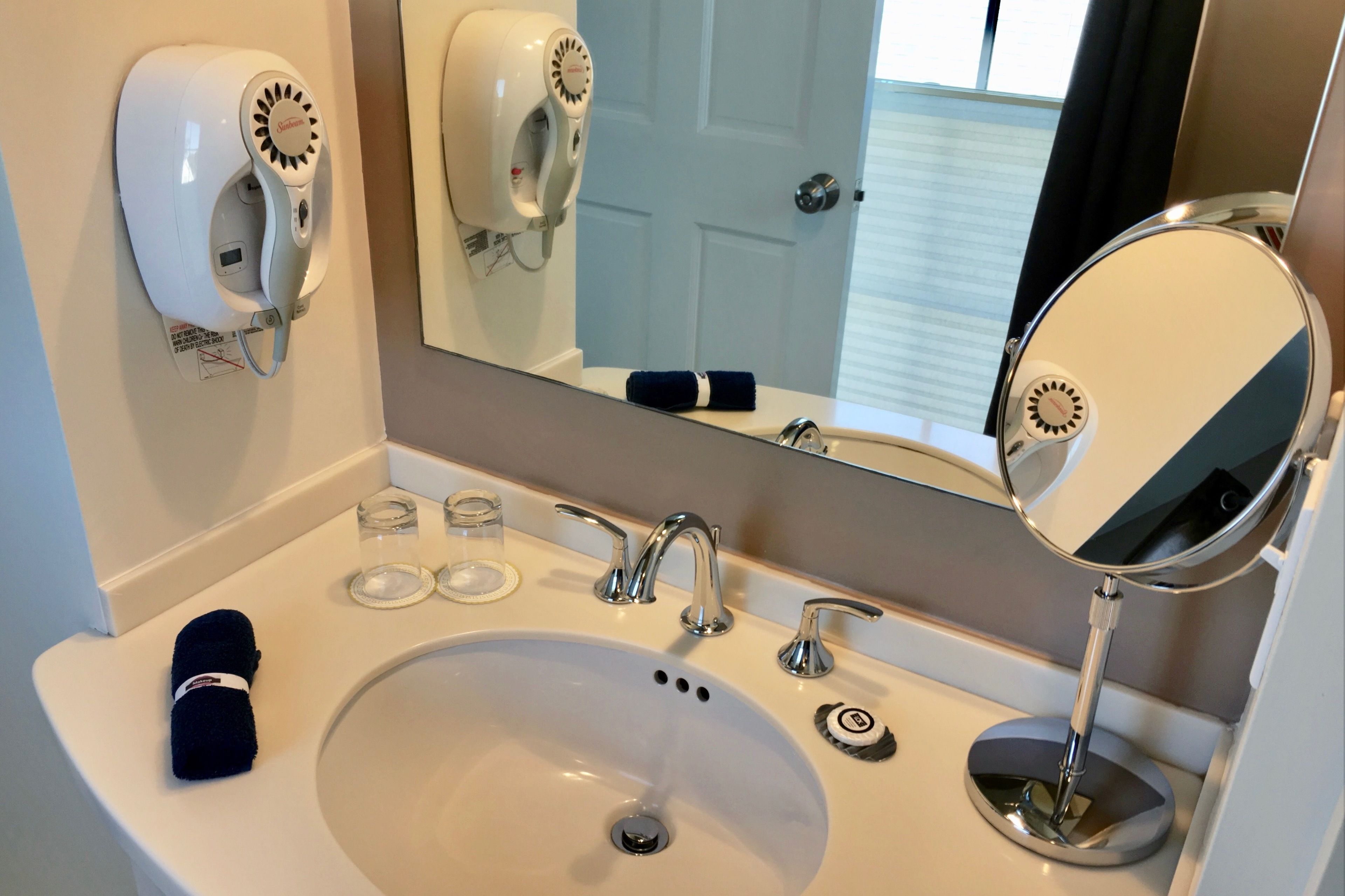 A bathroom with a sink, two hair dryers, a towel, and a mirror.