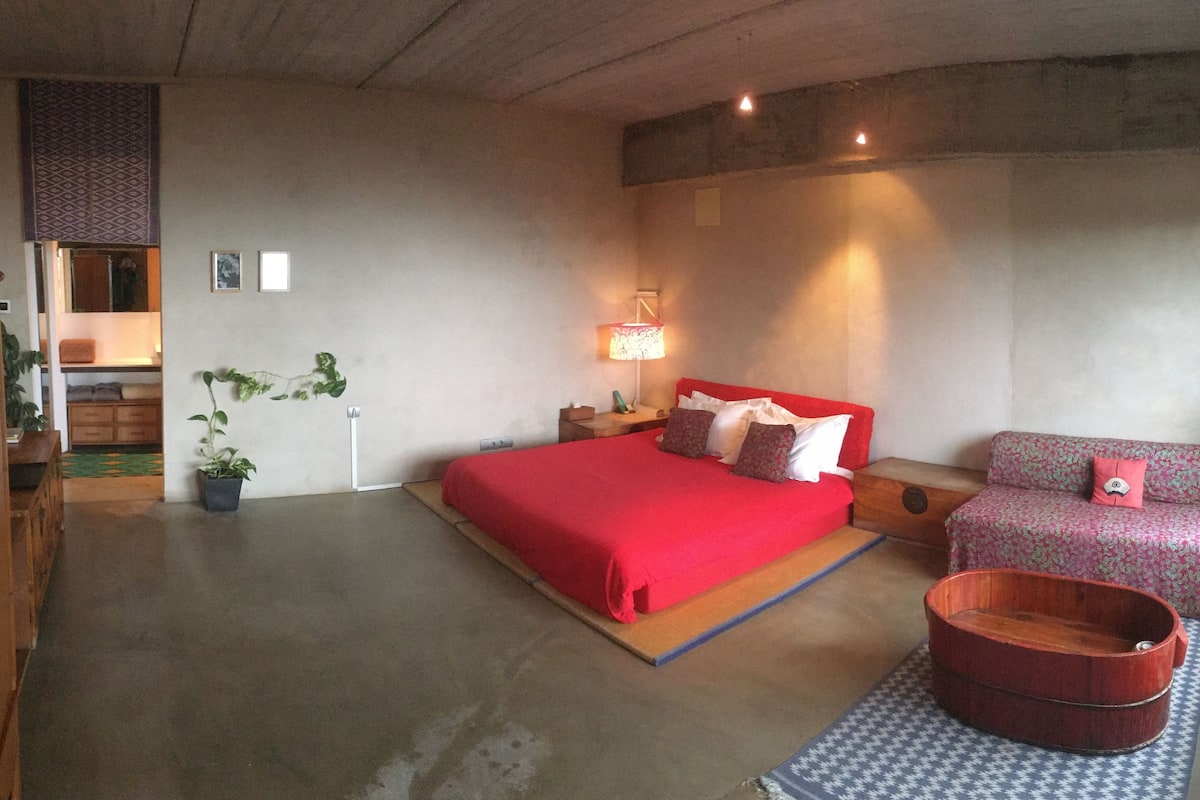 A bedroom with a large bed, a sofa, a wooden tub, and a patterned rug.