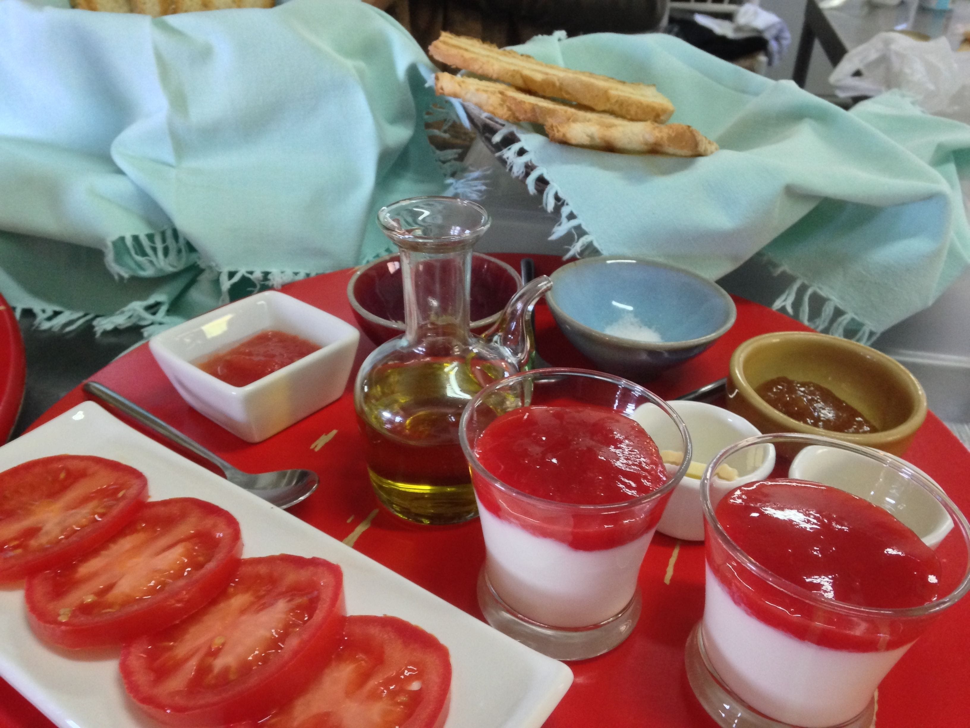 A table with a plate of tomato slices, a glass of red dessert, and various condiments.