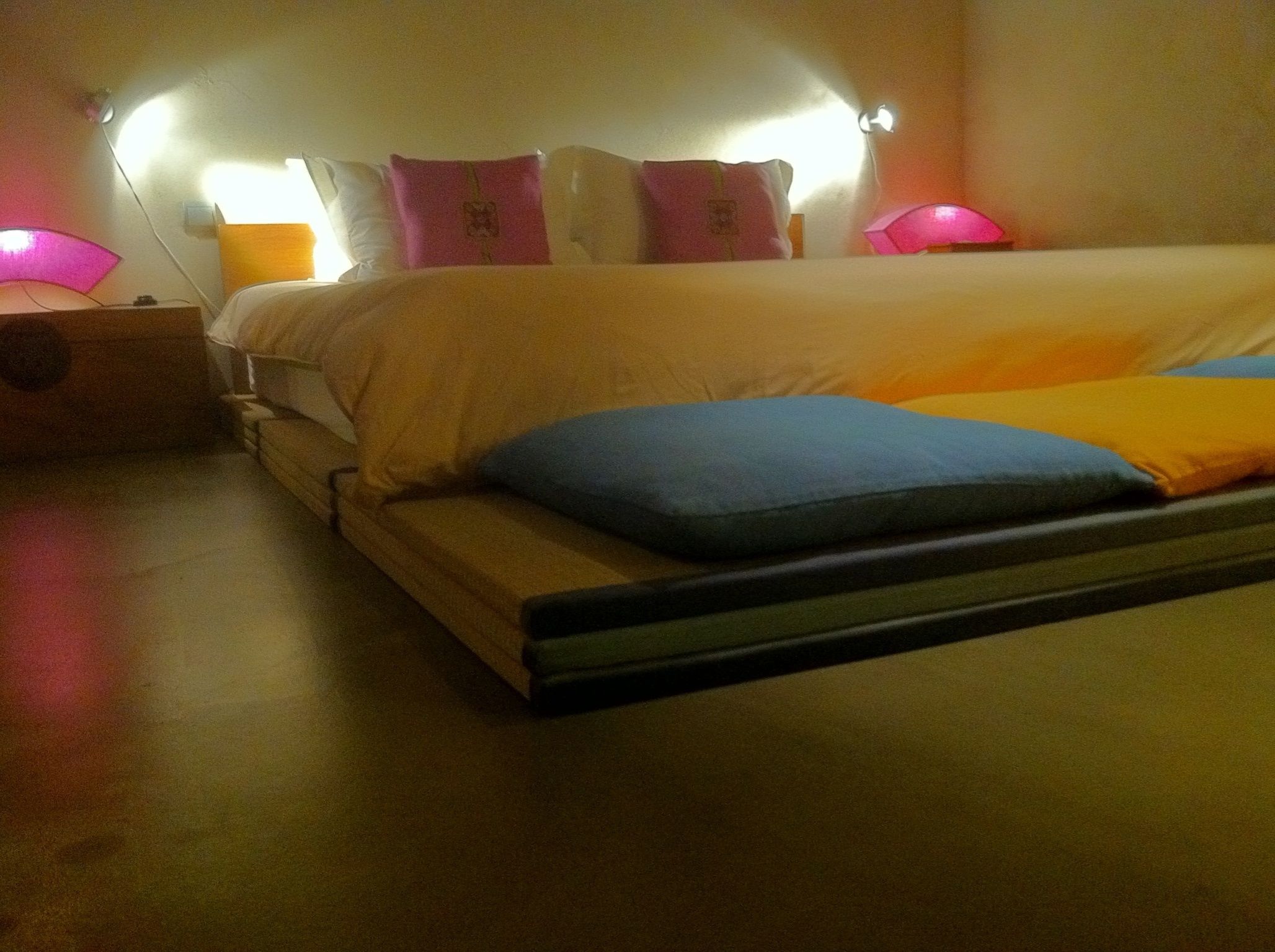 Un lit avec un matelas, des oreillers et une tête de lit. Il y a une table de chevet avec une lampe dessus.