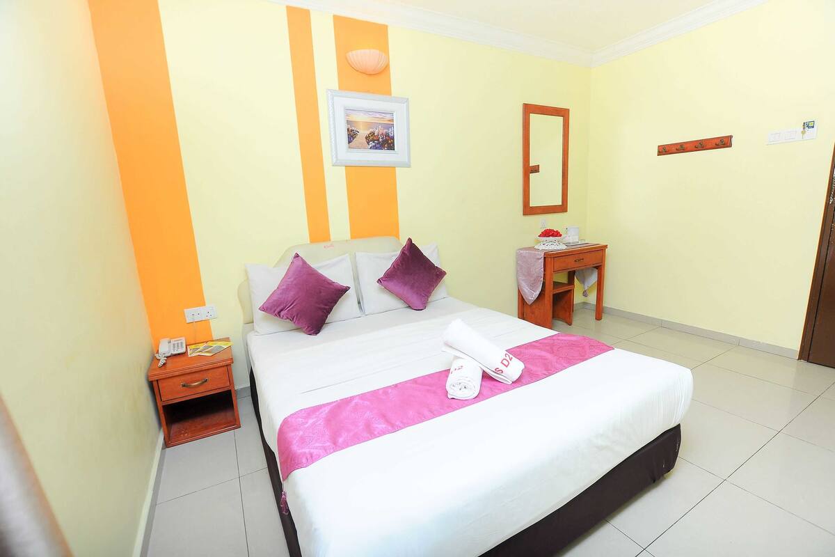 A hotel room with a bed, a nightstand, a small table, a mirror, and a picture on the wall.