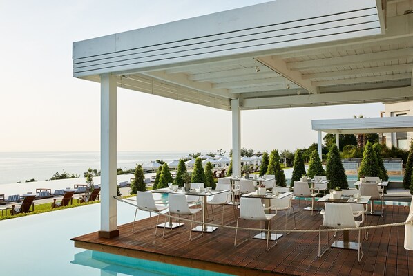 An outdoor pool area with lounge chairs and tables, overlooking a body of water.