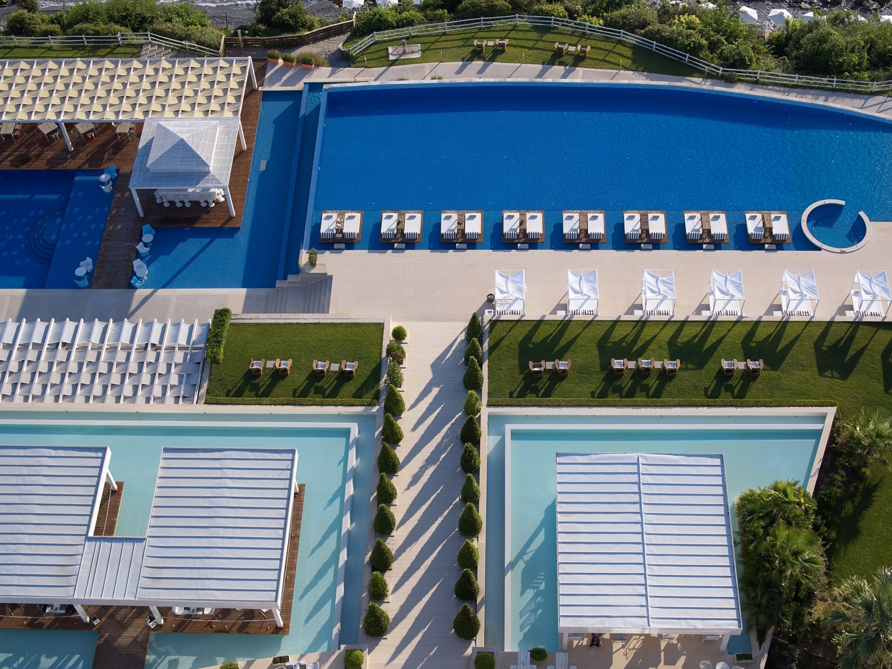 Vista aérea de un complejo turístico con múltiples piscinas, tumbonas y un césped bien cuidado.