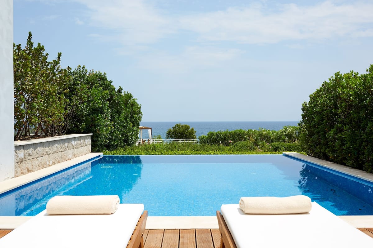 Ein Pool mit zwei Liegestühlen und Blick aufs Meer.