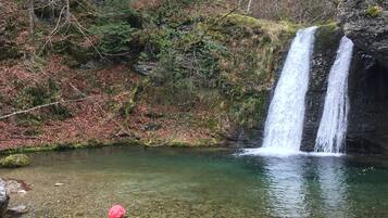 Una persona seduta su una roccia, vicino a un ruscello limpido, con una cascata sullo sfondo.