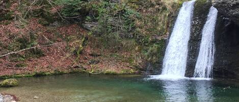 A person sitting on a rock by a clear stream with a waterfall in the background.
