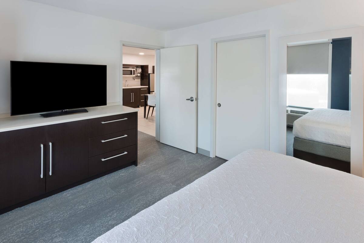 A modern hotel room with a flat-screen TV, a large bed, a wardrobe, and a door leading to a balcony.