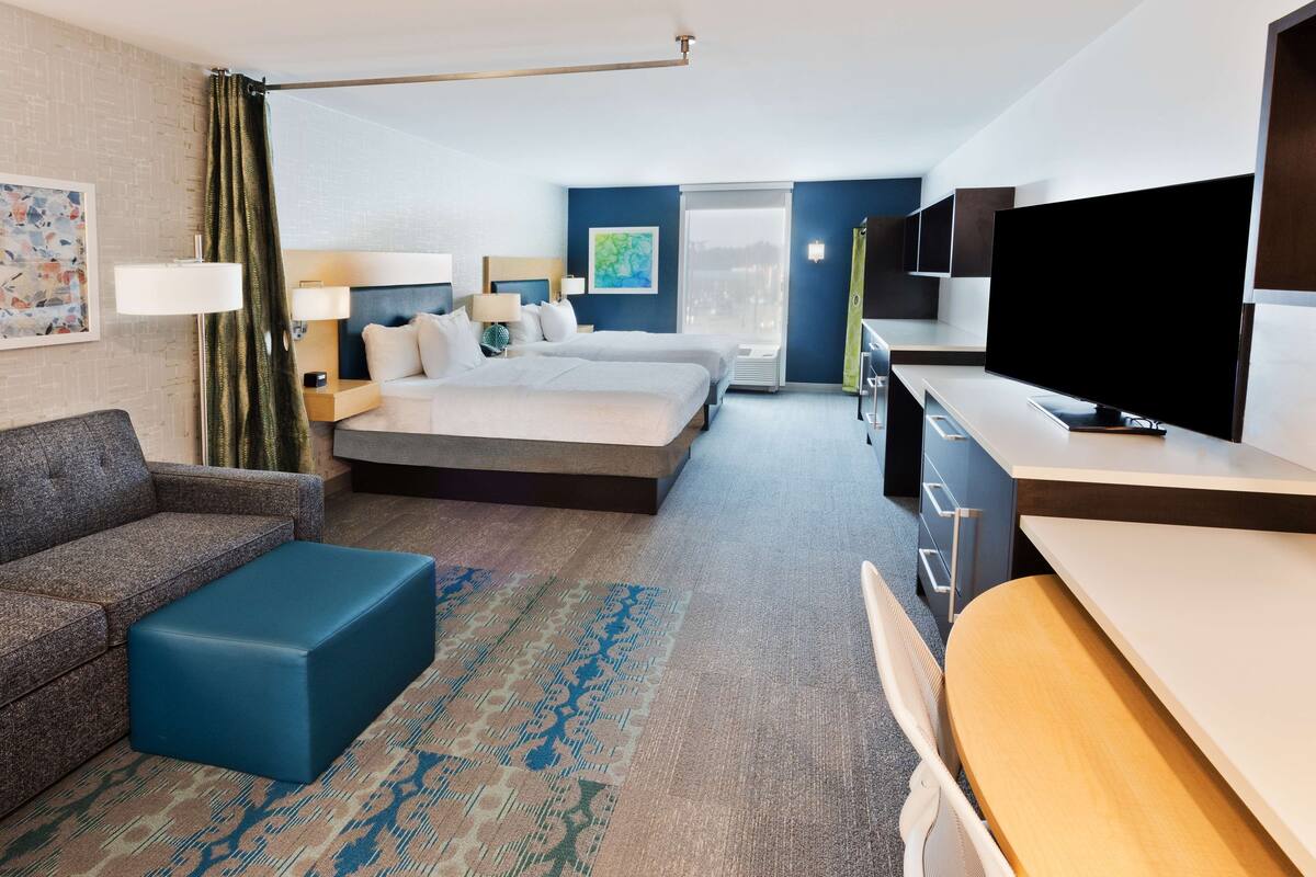 A modern hotel room with a large bed, a sofa, a desk, and a TV.