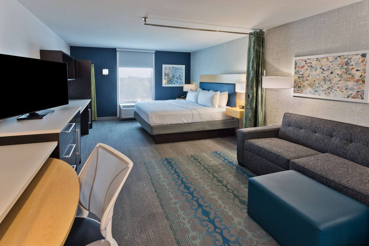 A hotel room with a bed, a desk with a TV, a sofa, and a chair.
