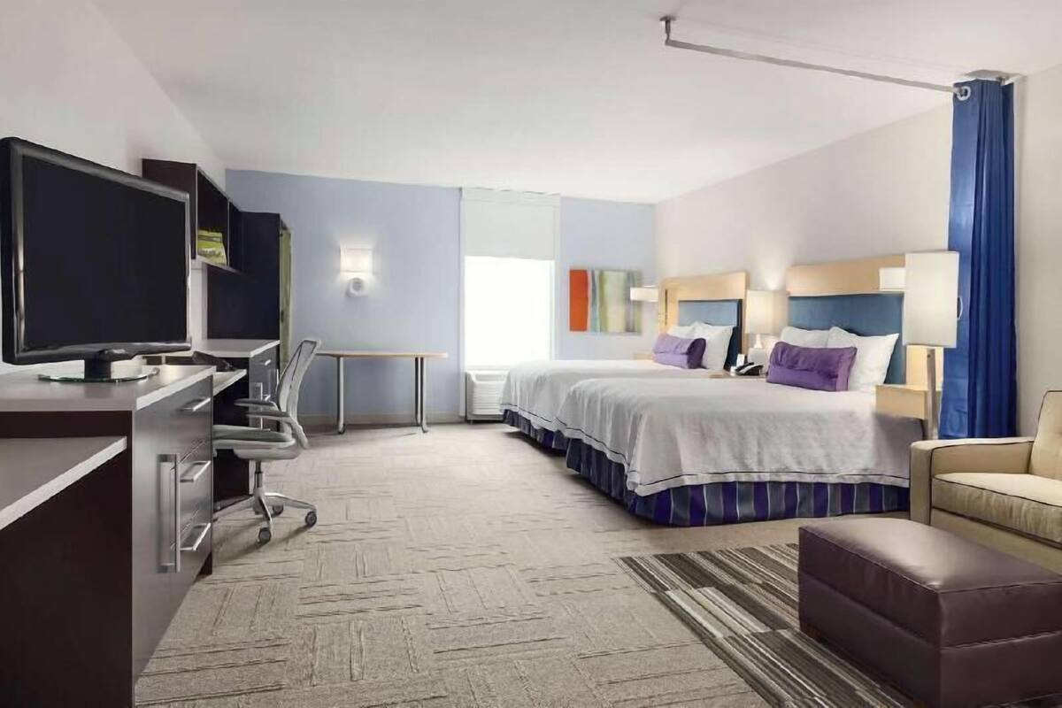 A hotel room with a bed, desk, chair, television, and a view of the outdoors.