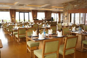 A hotel dining area with multiple tables, chairs, and a stone wall. - Hotel Tibet International (Kathmandu)