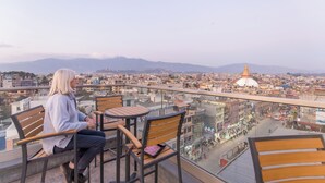 Una persona sentada en un balcón con vistas a un paisaje urbano, que incluye una cúpula destacada.