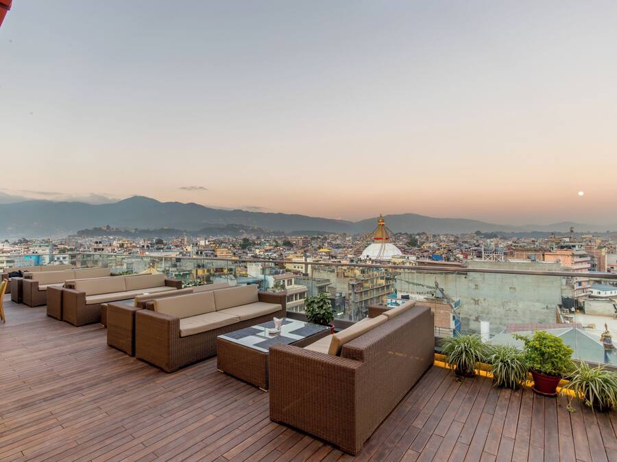 A rooftop terrace with wicker furniture and potted plants, overlooking a cityscape with a prominent dome structure.