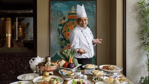 A chef standing in front of a table with various dishes and a traditional painting in the background. - Hotel Tibet (Kathmandu)