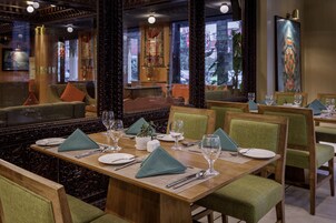 A restaurant with wooden tables, green upholstered chairs, and a decorative mirror.