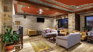 A spacious living room with a stone wall, multiple sofas, a flat-screen TV, and a large window offering a city view. - Hotel Tibet (Kathmandu)