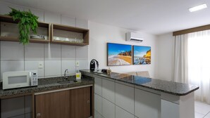 A modern kitchen with a microwave, coffee maker, and a plant. There are two framed pictures on the wall and an air conditioning unit. - Villa Park Hotel Natal (Natal)