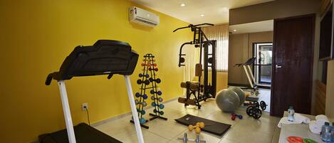 Un gimnasio en casa con cinta de correr, banco de pesas, mancuernas y pelotas de ejercicio.