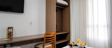 Une chambre d’hôtel comprenant un lit, une armoire en bois, un bureau avec une chaise, un téléviseur fixé au mur et une fenêtre avec des rideaux.