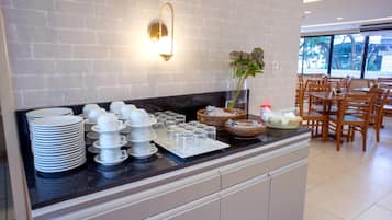 A buffet setup with stacked plates, bowls, and glasses on a counter, with a wall-mounted light fixture and a vase with flowers.