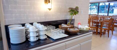 Una mesa de buffet con platos, tazones y vasos apilados, una lámpara de pared y un jarrón con flores.