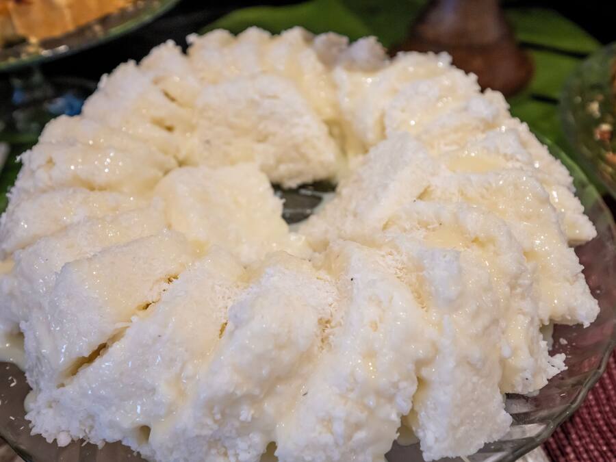 Un bol de vidrio con un postre blanco y cremoso, coronado con una capa caramelizada, sobre una mesa con una hoja verde debajo.