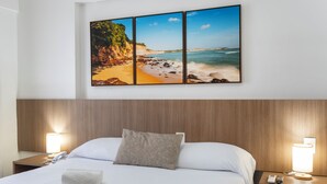A hotel room with a bed, a nightstand with a lamp, and a wall-mounted picture of a beach scene. - Villa Park Hotel Natal (Natal)