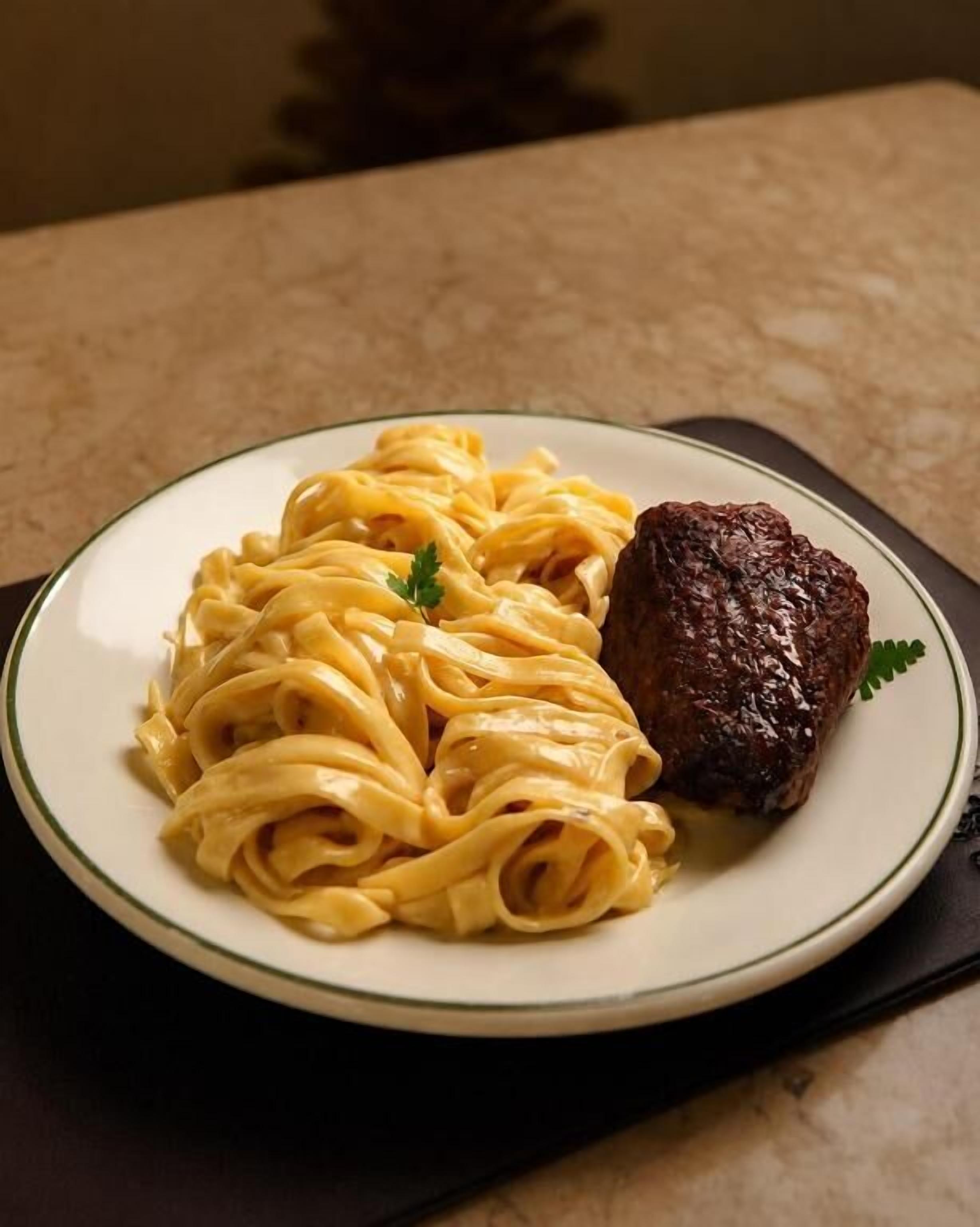 A plate of pasta and a steak on a table.