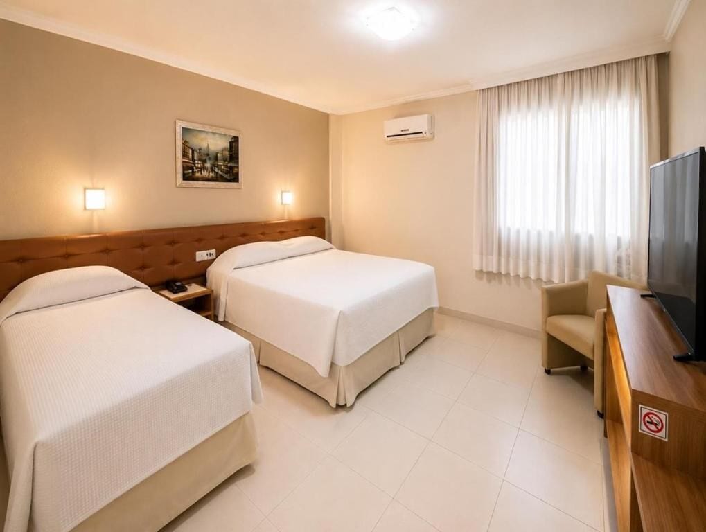 A hotel room with two beds, a television, a desk, and a painting on the wall.